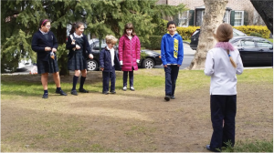 Five children face another child with her back facing the camera, playing a game in a neighborhood field.